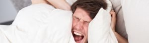 Man trying to block out the sound of a squeaking bed with pillows.