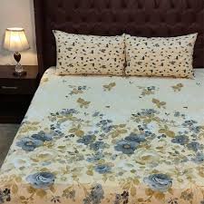 Cream floral bed sheet with blue and beige flower patterns, paired with matching pillowcases on a tufted headboard in a cozy bedroom.