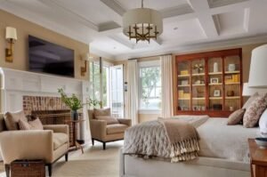 Elegant guest bedroom with a upholstered bed, cozy armchairs, fireplace, layered bedding, and warm neutral décor.