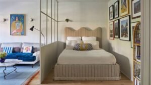 Compact studio apartment featuring a cozy bed separated from the living area by a glass partition, with gallery wall art, a modern sofa, and space-saving interior design.