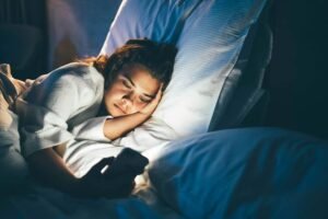 Person lying in bed using a smartphone at night, illustrating how screen time and blue light exposure before bedtime can disrupt sleep.