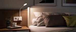 Modern bedroom with a wall-mounted LED reading lamp illuminating a cozy bed and bedside table, creating a warm and relaxing nighttime atmosphere.