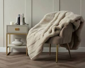 Soft faux fur throw blanket draped over an accent chair beside a modern bedside table in a neutral bedroom.