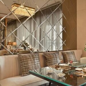Elegant dining area featuring a mirrored accent wall, upholstered bench seating, a glass-top dining table, decorative cushions, and a crystal chandelier in a contemporary luxury interior.