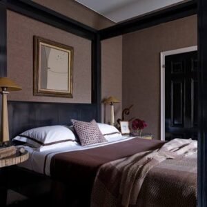 Elegant guest bedroom featuring a dark wood bed, layered neutral bedding, decorative pillows, bedside lamps, and warm earth-tone décor.