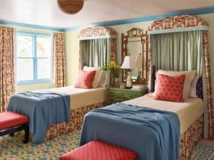 Twin guest bedroom featuring two upholstered canopy-style beds with floral fabric, blue throws, matching bedside table, and colorful traditional décor.
