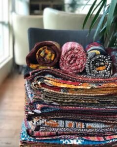 Stack of colorful folded throw blankets with different textures, patterns, and fabrics arranged on a chair.