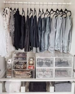 Well-organized wardrobe featuring color-coordinated clothing on slim black velvet hangers, clear acrylic storage drawers for accessories, and neatly folded garments on shelves.