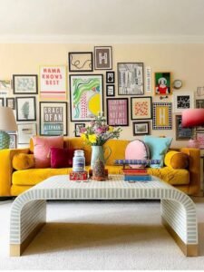 Colorful eclectic living room featuring a mustard yellow velvet sofa, vibrant throw pillows, a gallery wall of framed artwork, and a modern striped coffee table with fresh flowers.