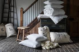 A rustic bedroom scene featuring stacked white pillows, folded bedding, decorative cushions, a wooden staircase, and vintage-style furniture in a cozy farmhouse setting.