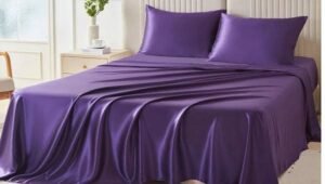 Purple satin bed sheet set with matching pillowcases on a modern upholstered bed, creating a luxurious and elegant bedroom atmosphere.