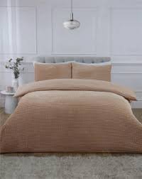 Beige waffle-textured duvet cover set on a neatly made bed in a minimalist white bedroom with neutral décor and soft natural lighting.