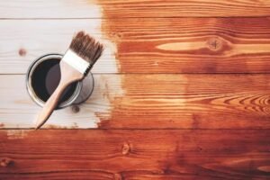 Applying a natural wood finish to a wooden surface with a brush to enhance the wood grain and protect the timber.